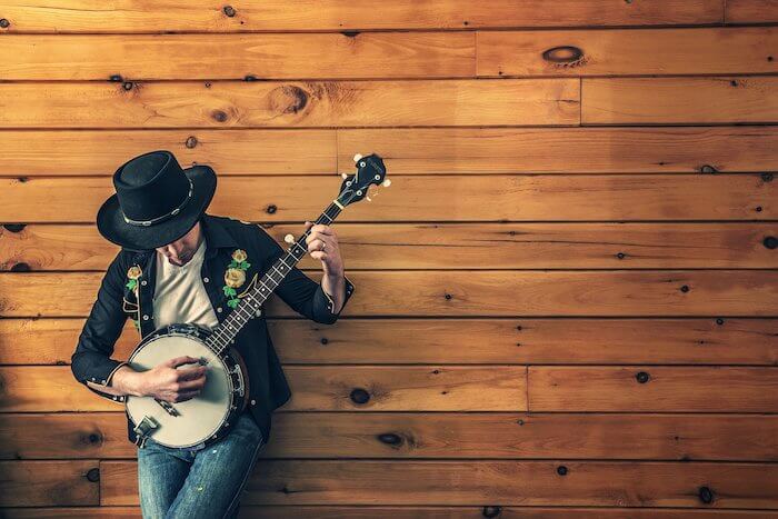 茶色い木の壁にもたれかかったギターを持った人