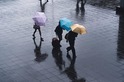 雨の中傘をさして歩く三人の人
