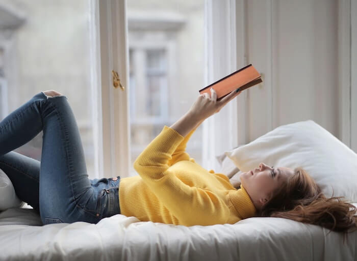 ベッドに寝転んで本を読む女性