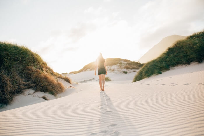 白い砂の上を歩く女性の後ろ姿